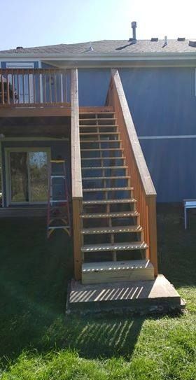 Wooden deck stairs leading down from a blue house to a grassy yard.