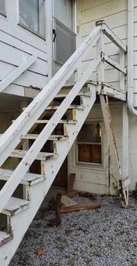 White wooden exterior stairs with peeling paint, leading to a doorway.