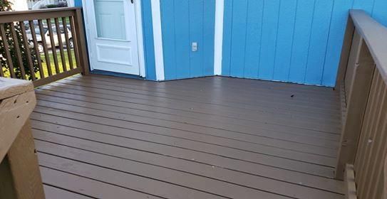 Brown deck with railing attached to a blue house with a white door.