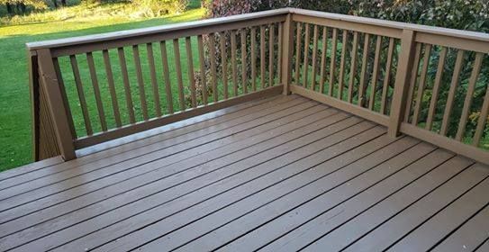 Wooden deck with railing, brown stained planks and green lawn background.