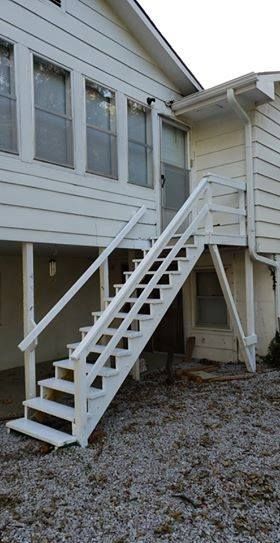 White wooden outdoor staircase leading up to a door on a white building.