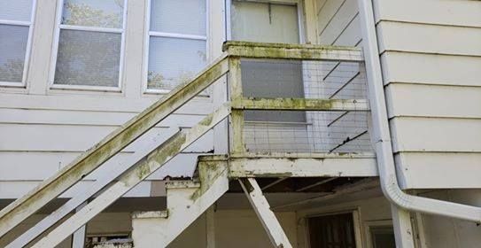 Exterior staircase with green mildew, leading to a doorway and windows on a white house.