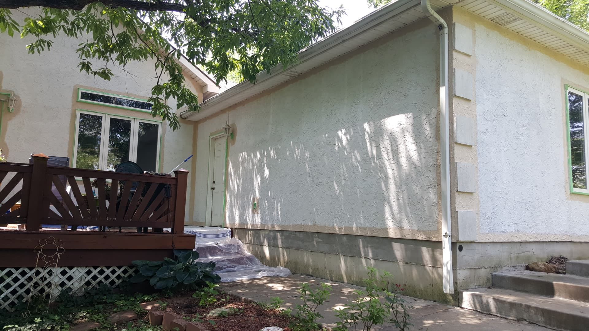 Exterior of a stucco house with a wooden deck and steps leading up. Trees and sky visible.