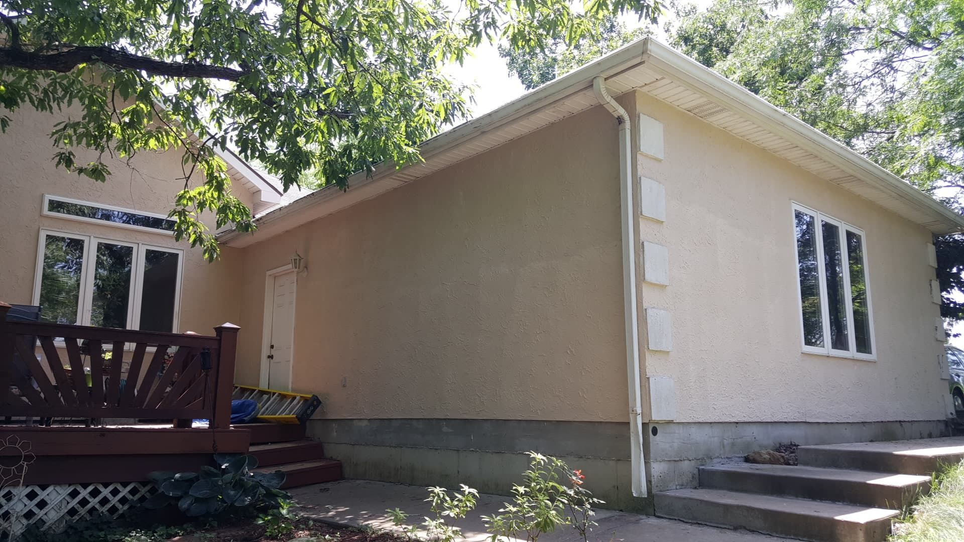 Tan stucco building with white trim, steps leading up, and trees overhead.