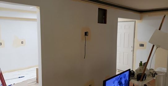 Interior renovation: wall with exposed wiring, doorways, and a TV in a room under construction.