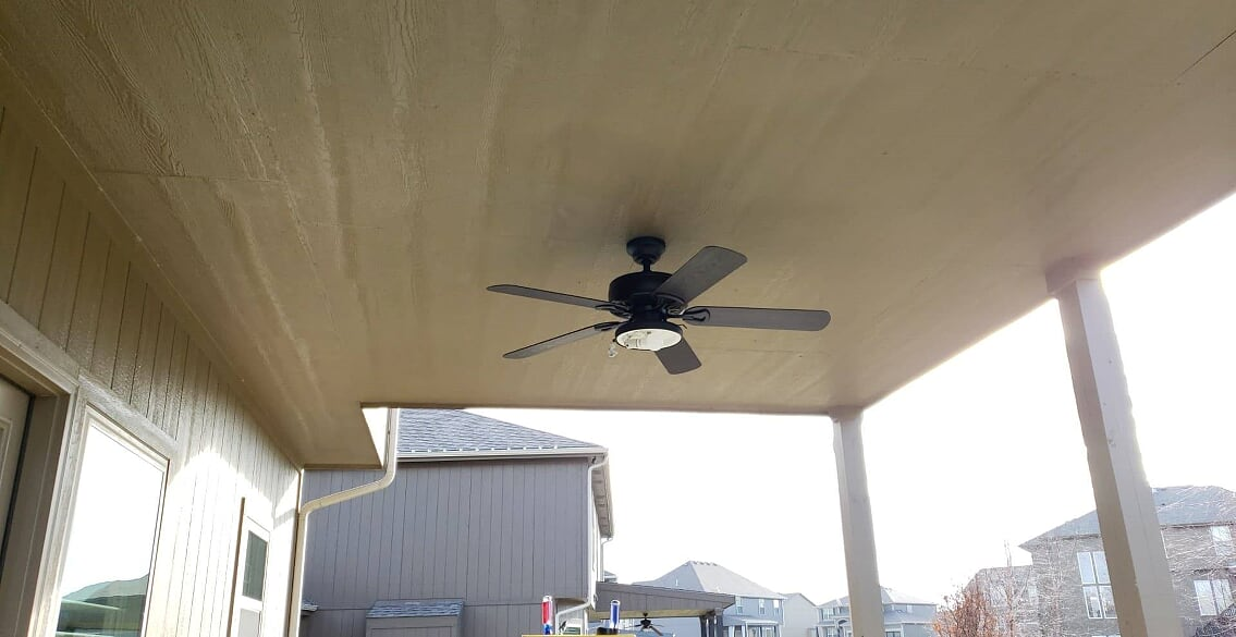 Ceiling fan on an outdoor covered patio with houses in the background.