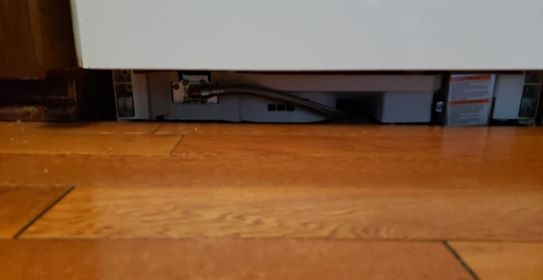 View of dishwasher's undercarriage against a wooden floor; wires and vents are visible.