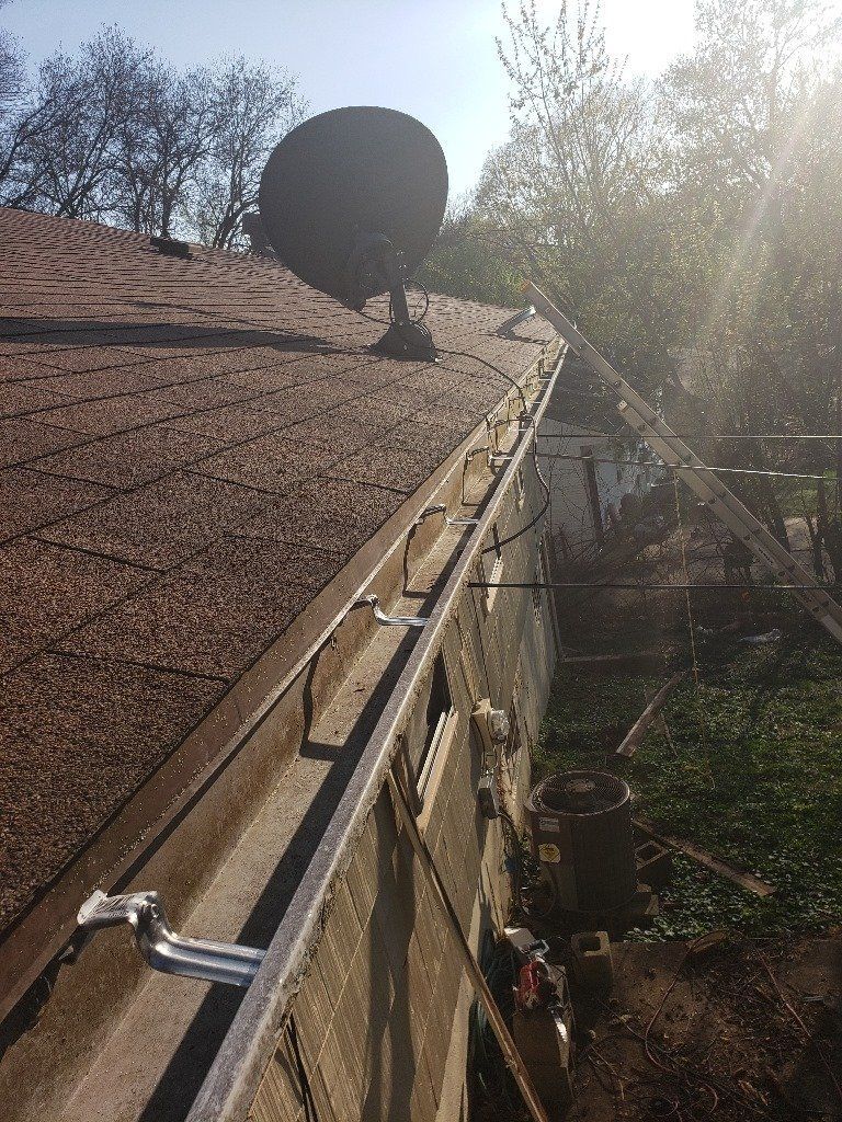 Gutter of a house with a satellite dish and ladder. Sunlight shines on the scene.