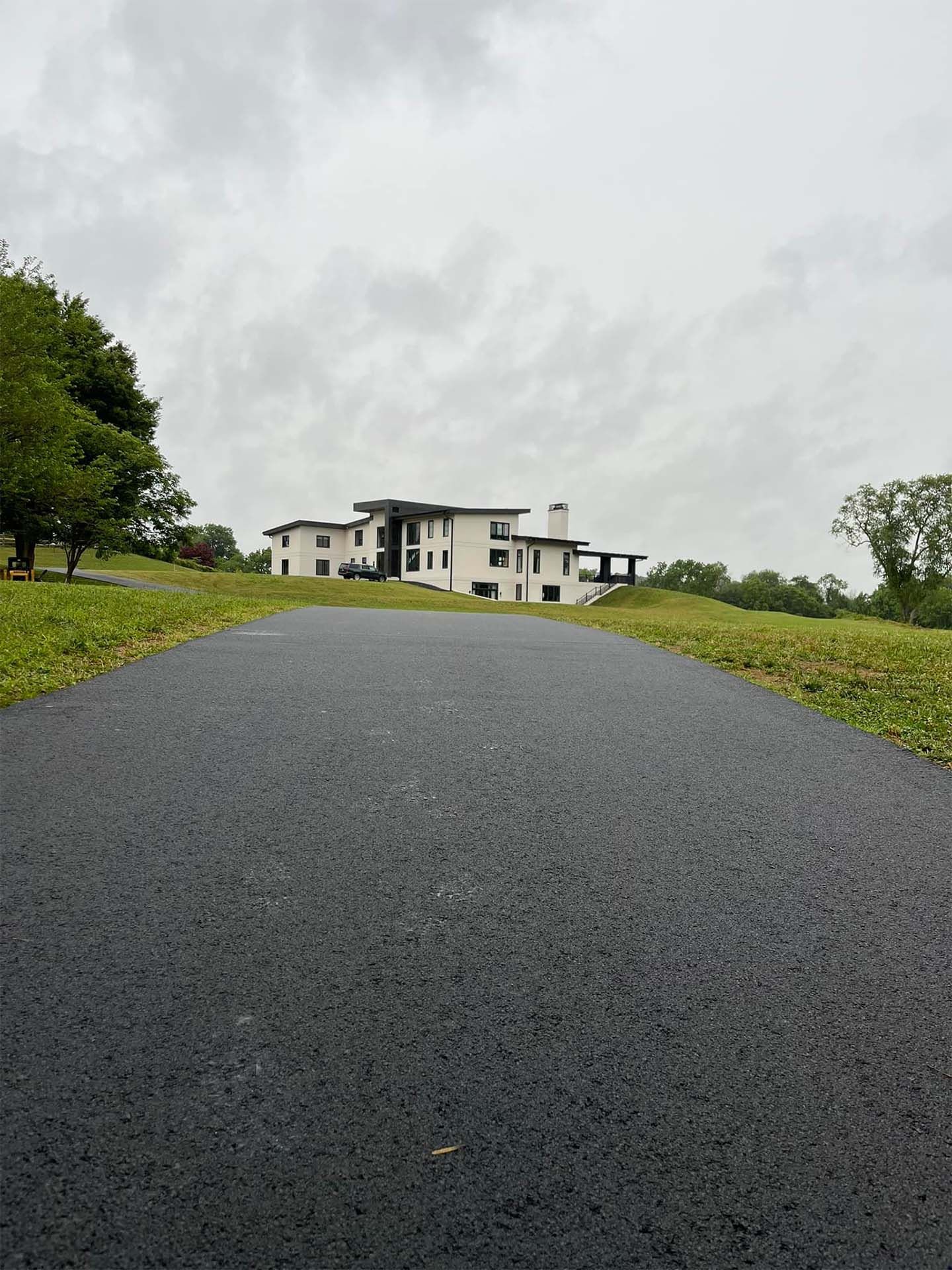A large white house is sitting on top of a grassy hill next to a road