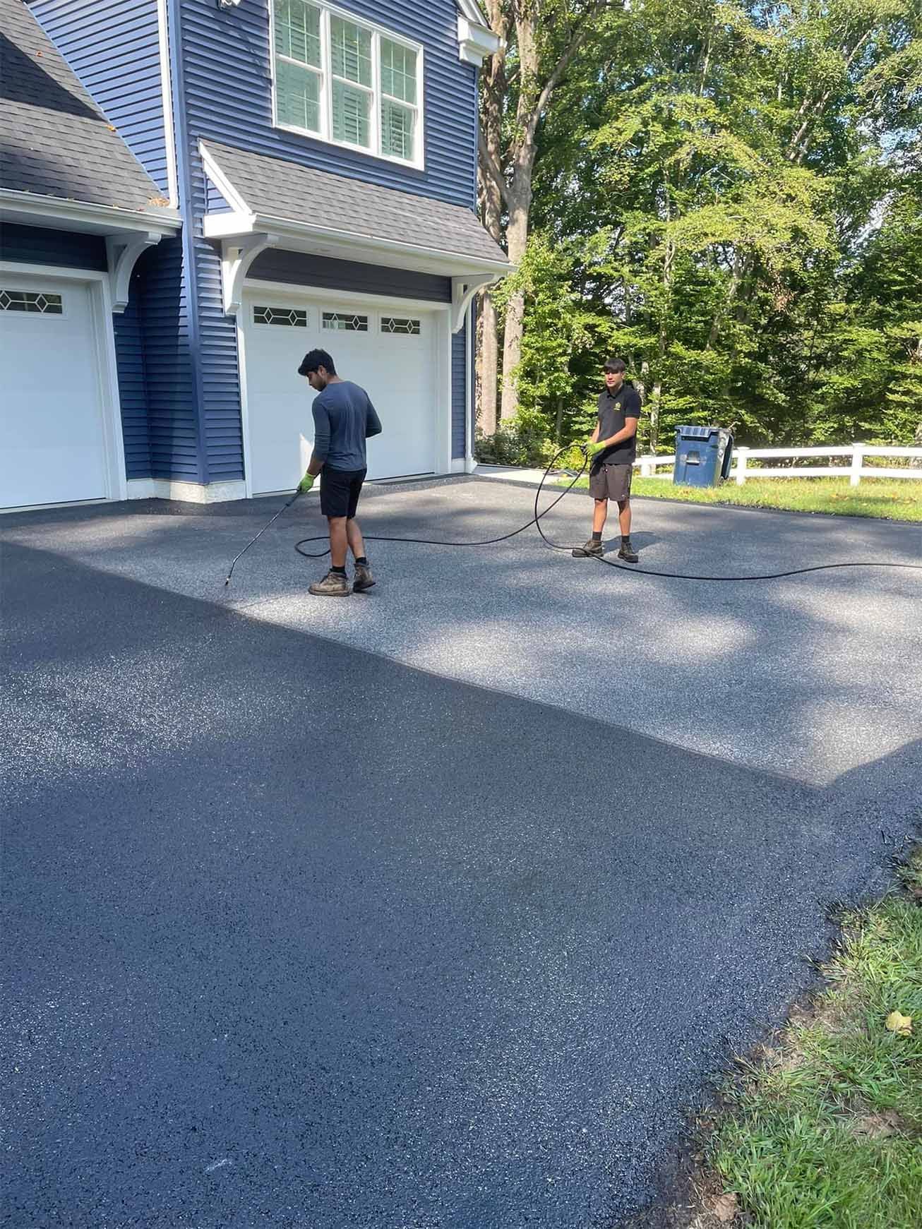 Two men are working on a driveway in front of a house