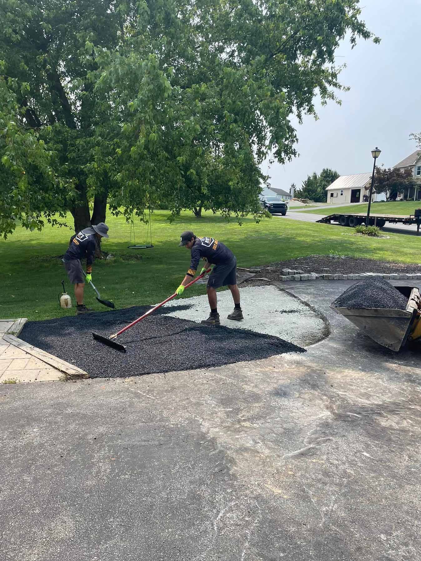 Two men are raking gravel in a driveway