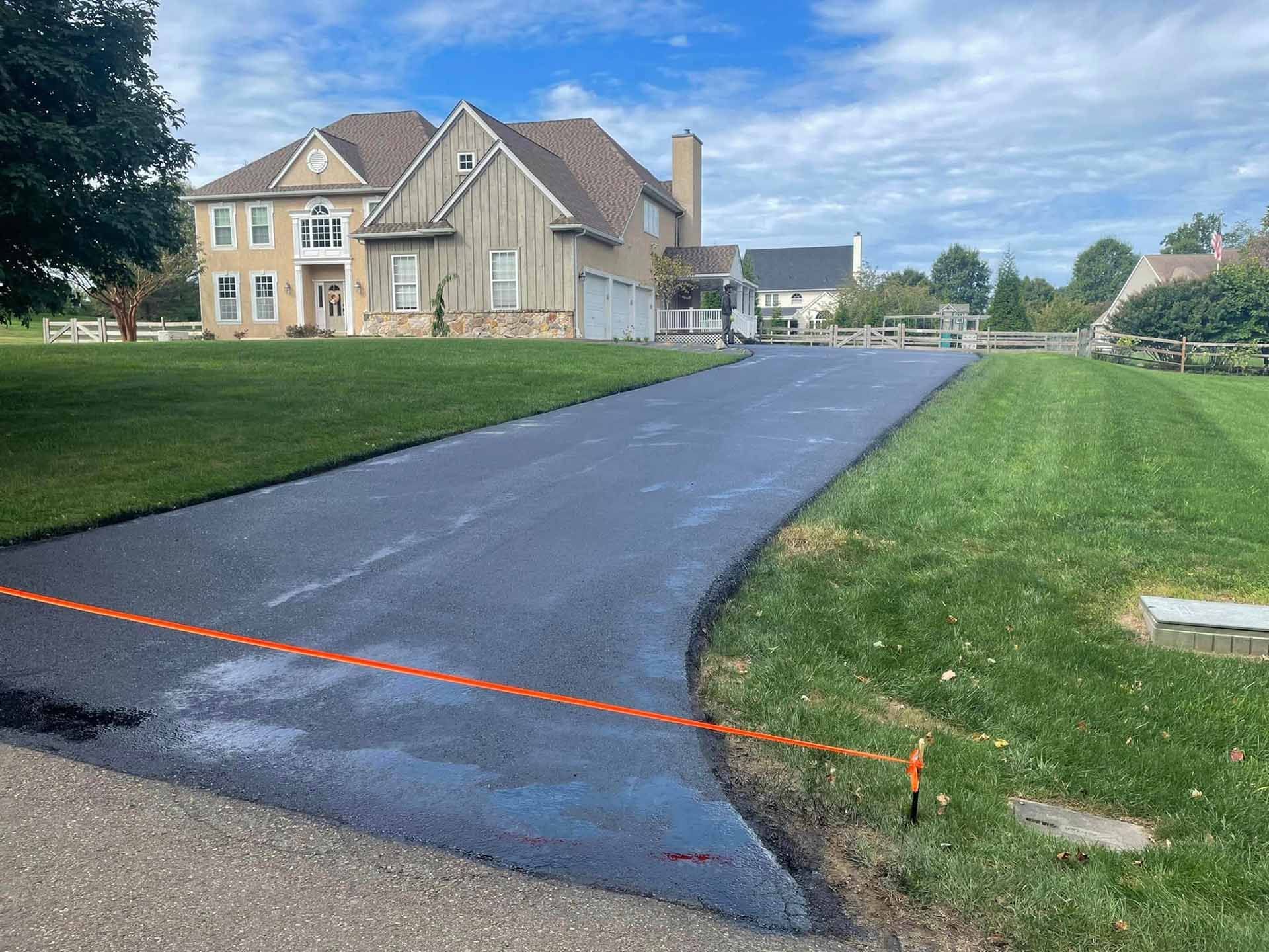 A large house is sitting on top of a lush green field next to a paved driveway