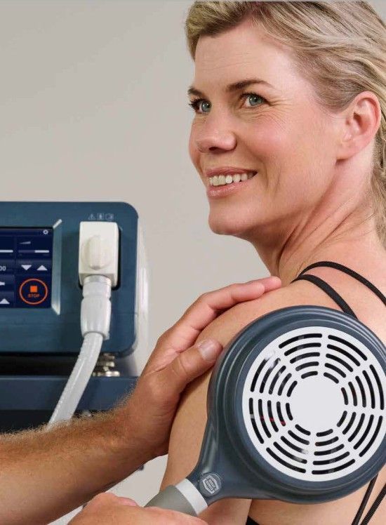 Woman receiving shoulder treatment with a medical device. Therapist's hand holds applicator.
