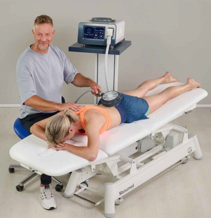 Therapist using a device on a patient's back on a treatment table. Gray machine, smiling.