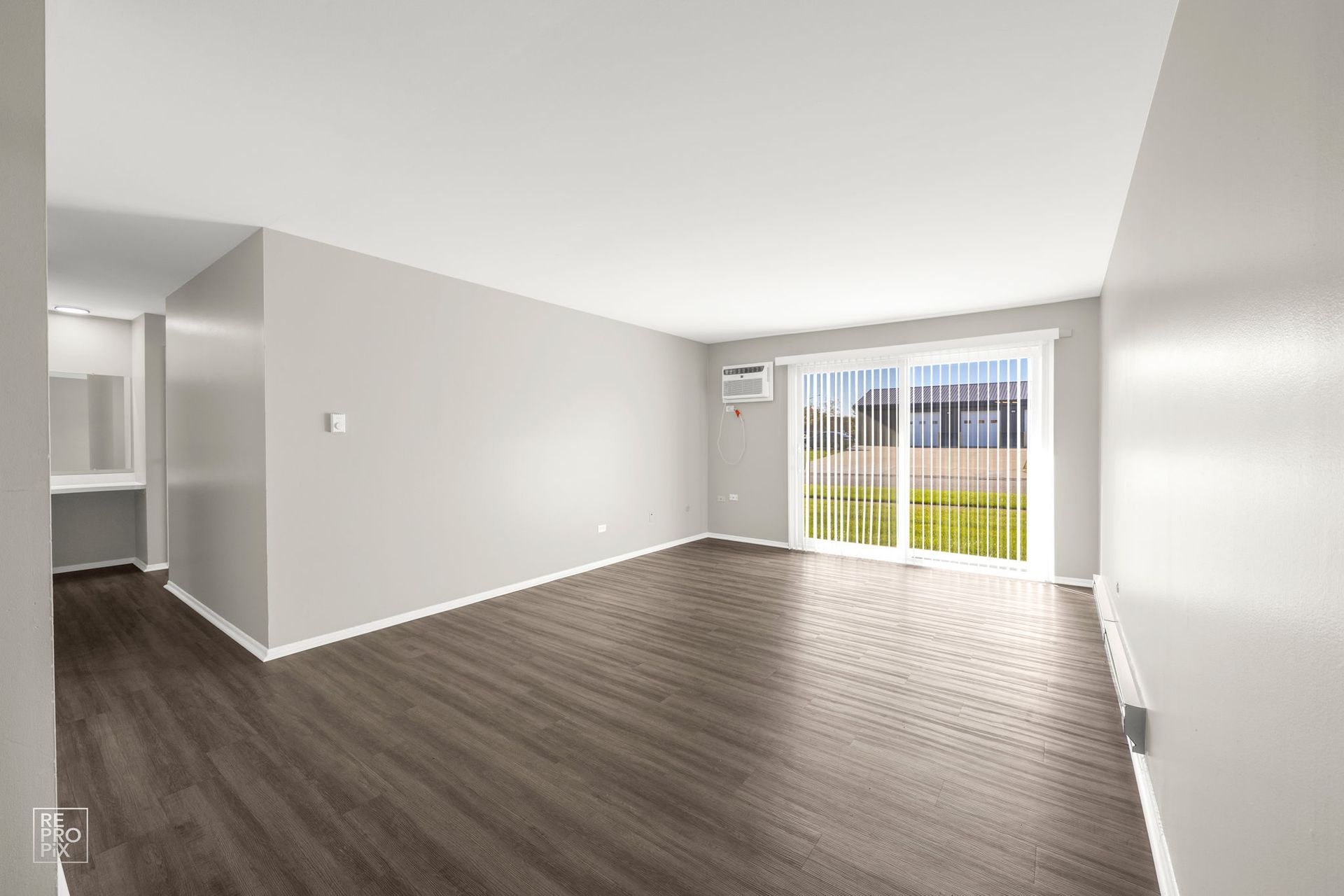 Empty, light-filled living room with wood-look floors, large sliding glass door, and gray walls.