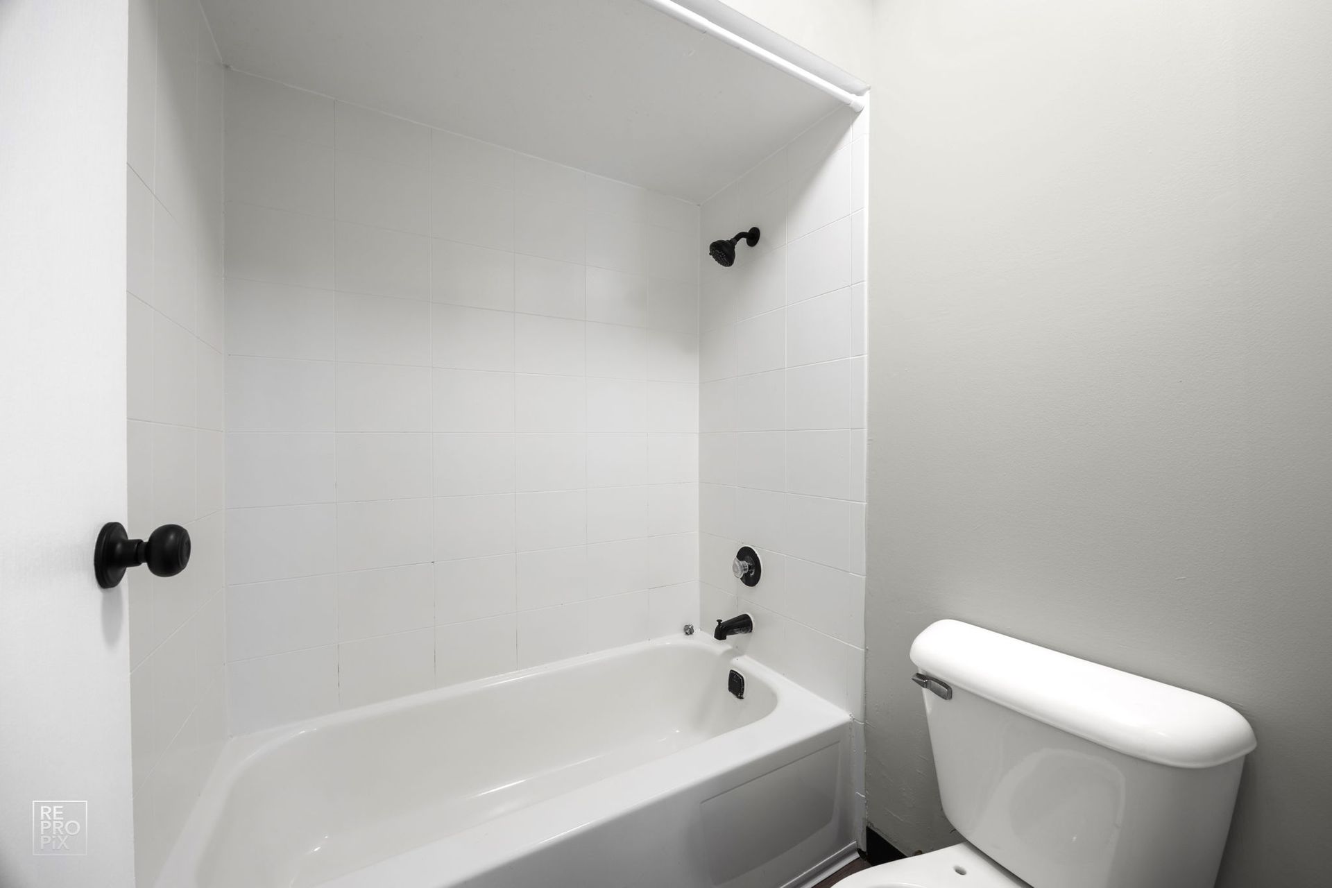 White bathroom with a tub, shower fixtures, and toilet. Gray wall on the right.