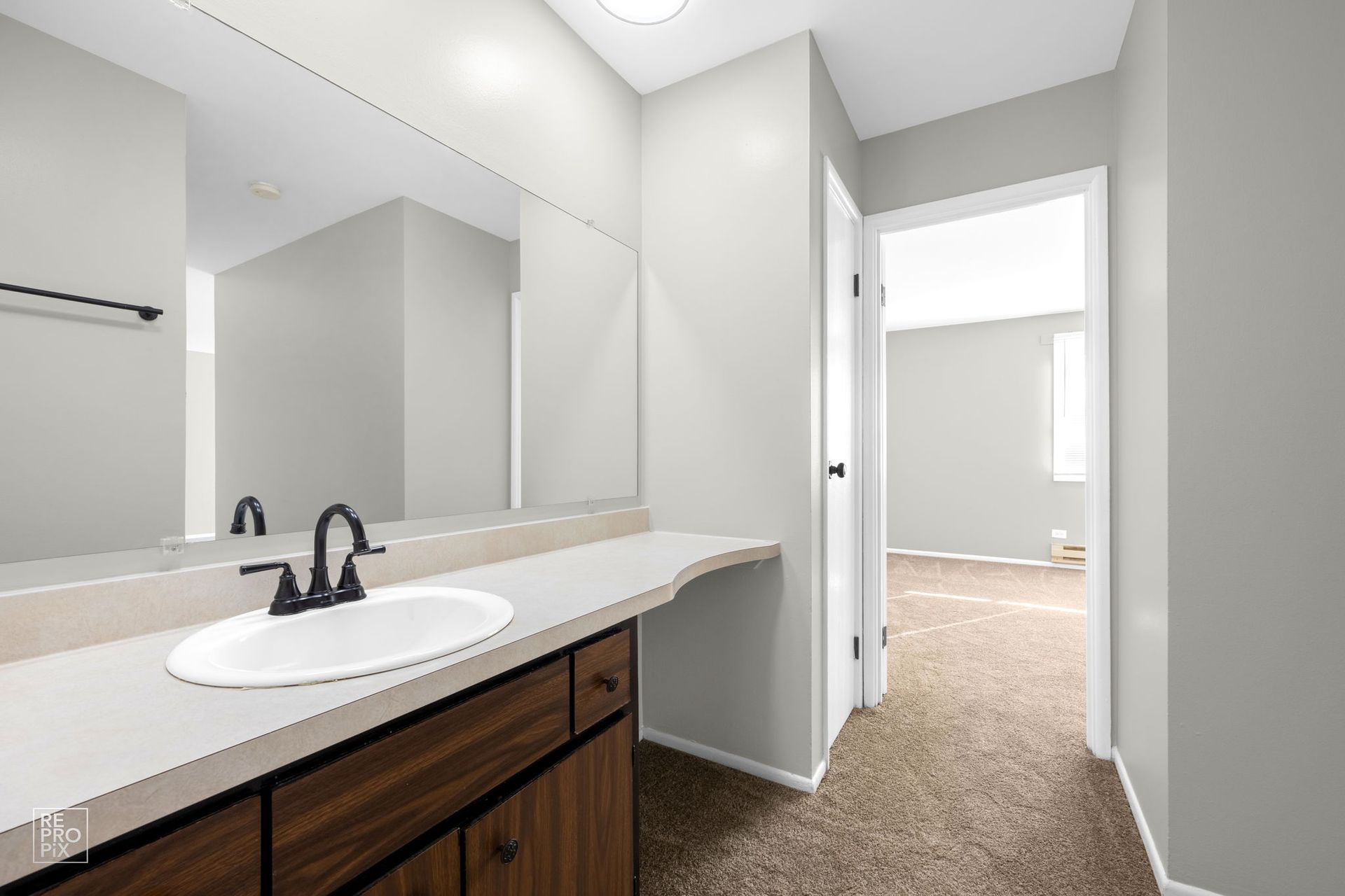 Bathroom with a dark vanity, white countertop, large mirror, and doorway to another room.