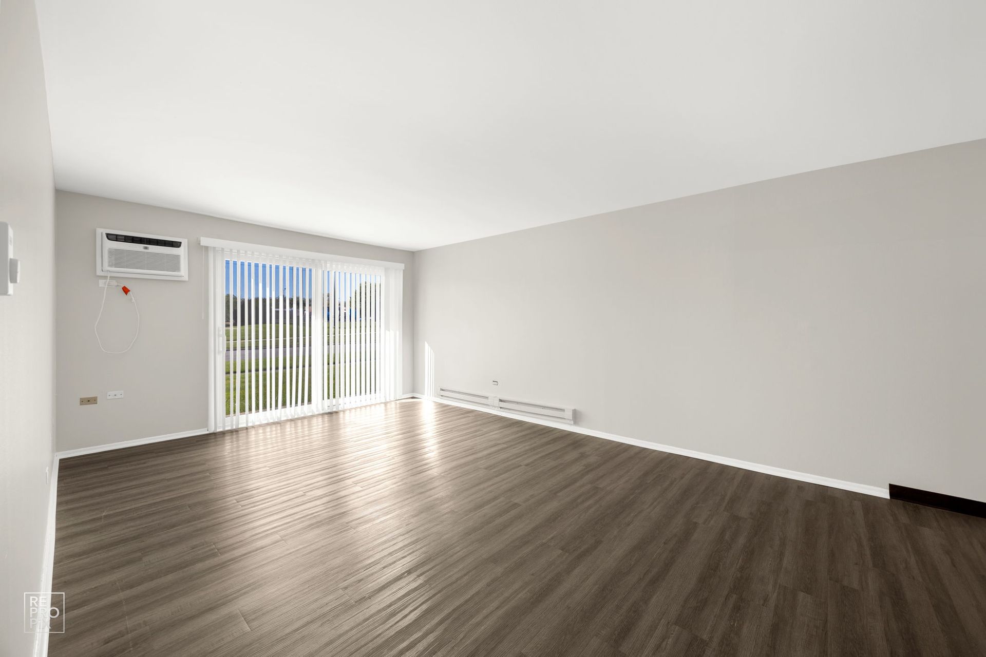Empty living room with wood floor, sliding door, and air conditioner.