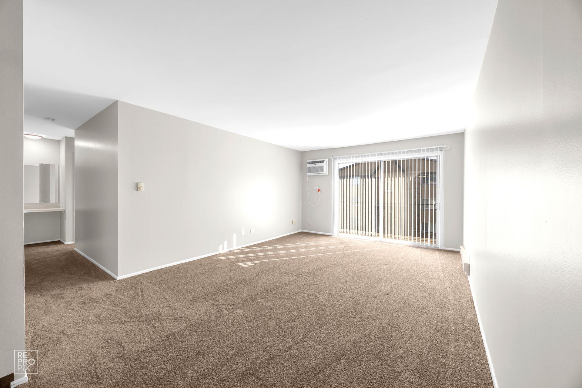 Empty living room with brown carpet, sliding glass door, and white walls.