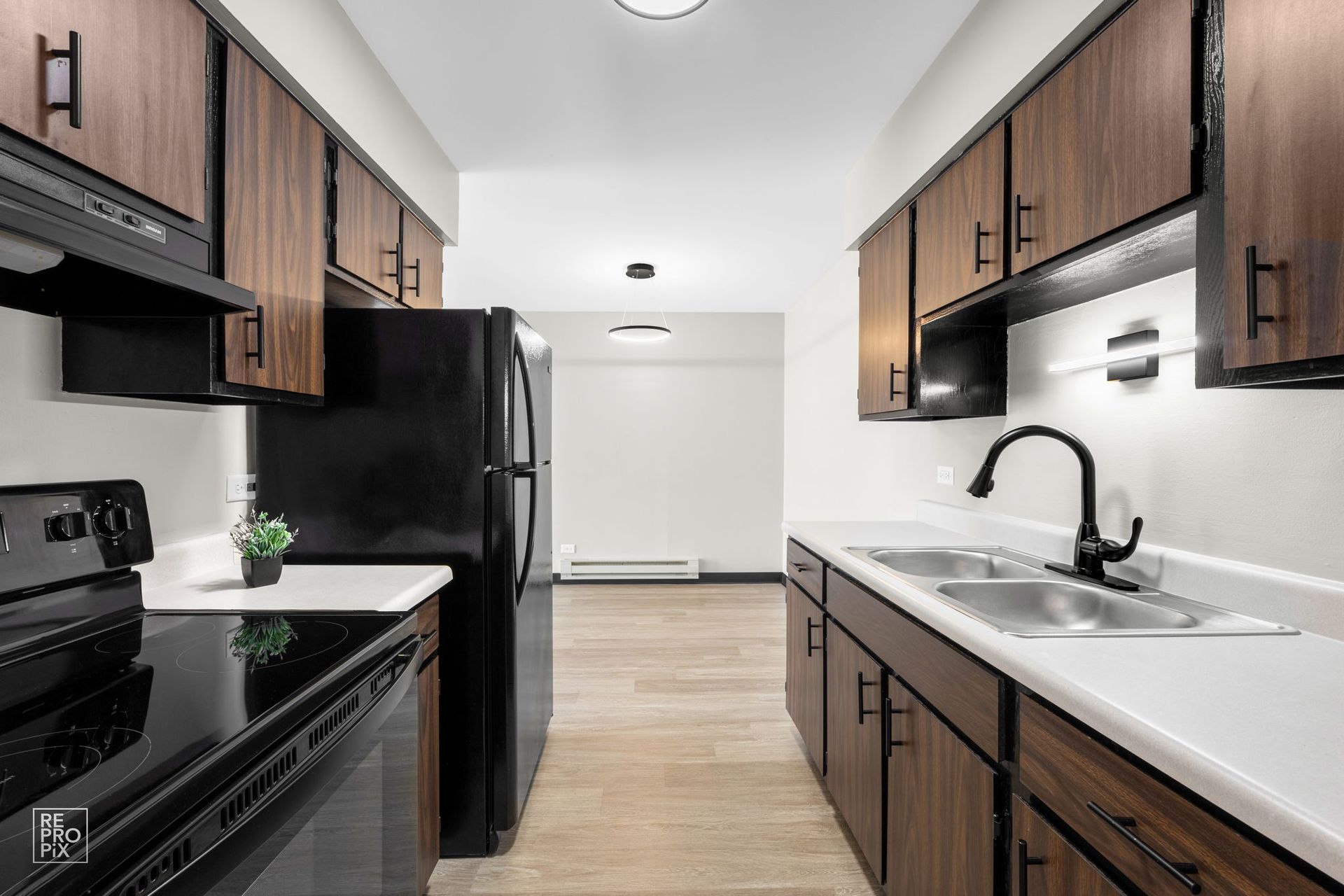 Narrow kitchen with dark wood cabinets, black appliances, and a white countertop.