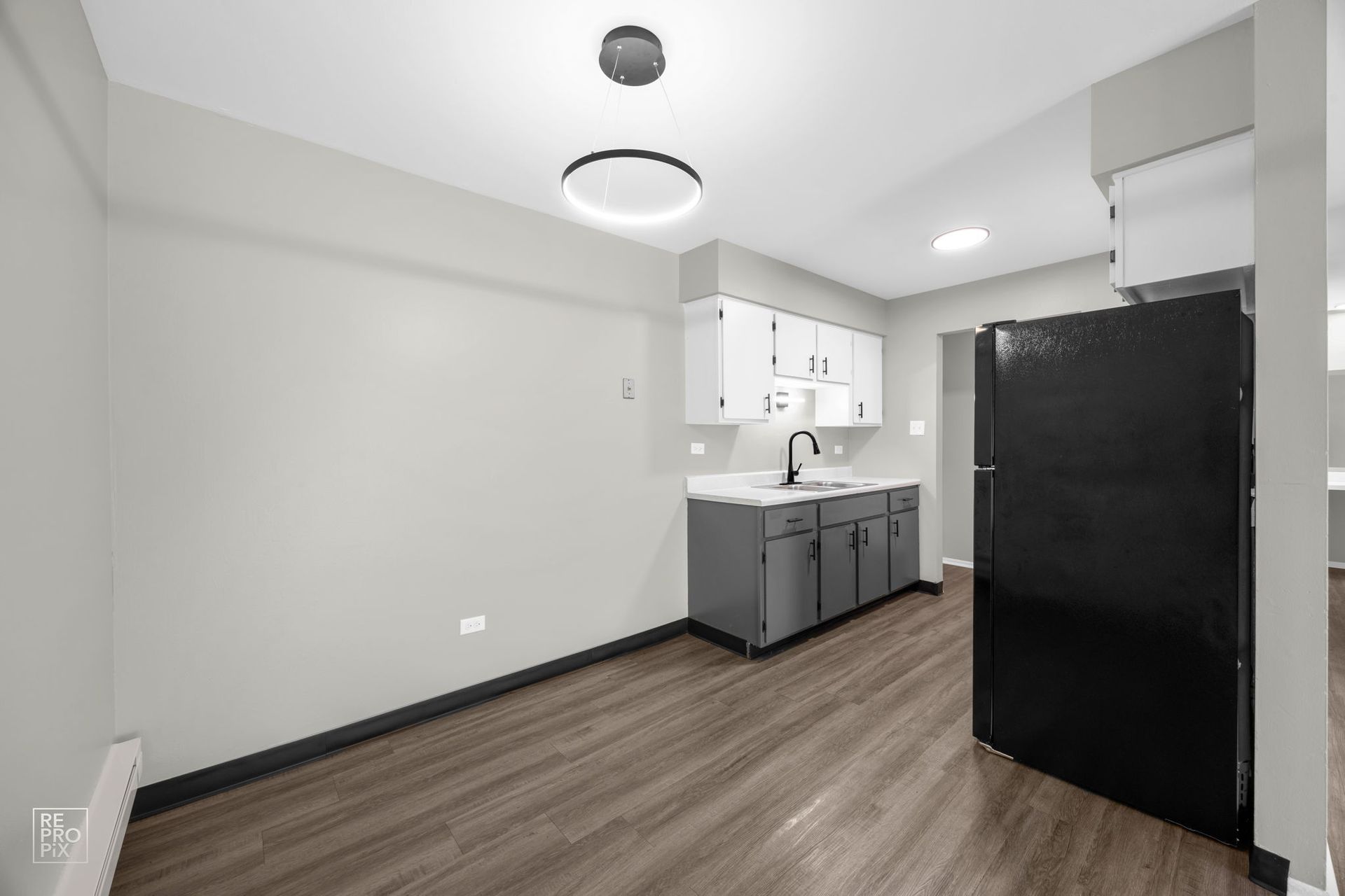 Empty kitchen with gray cabinets, black fridge, white countertops, and gray walls.