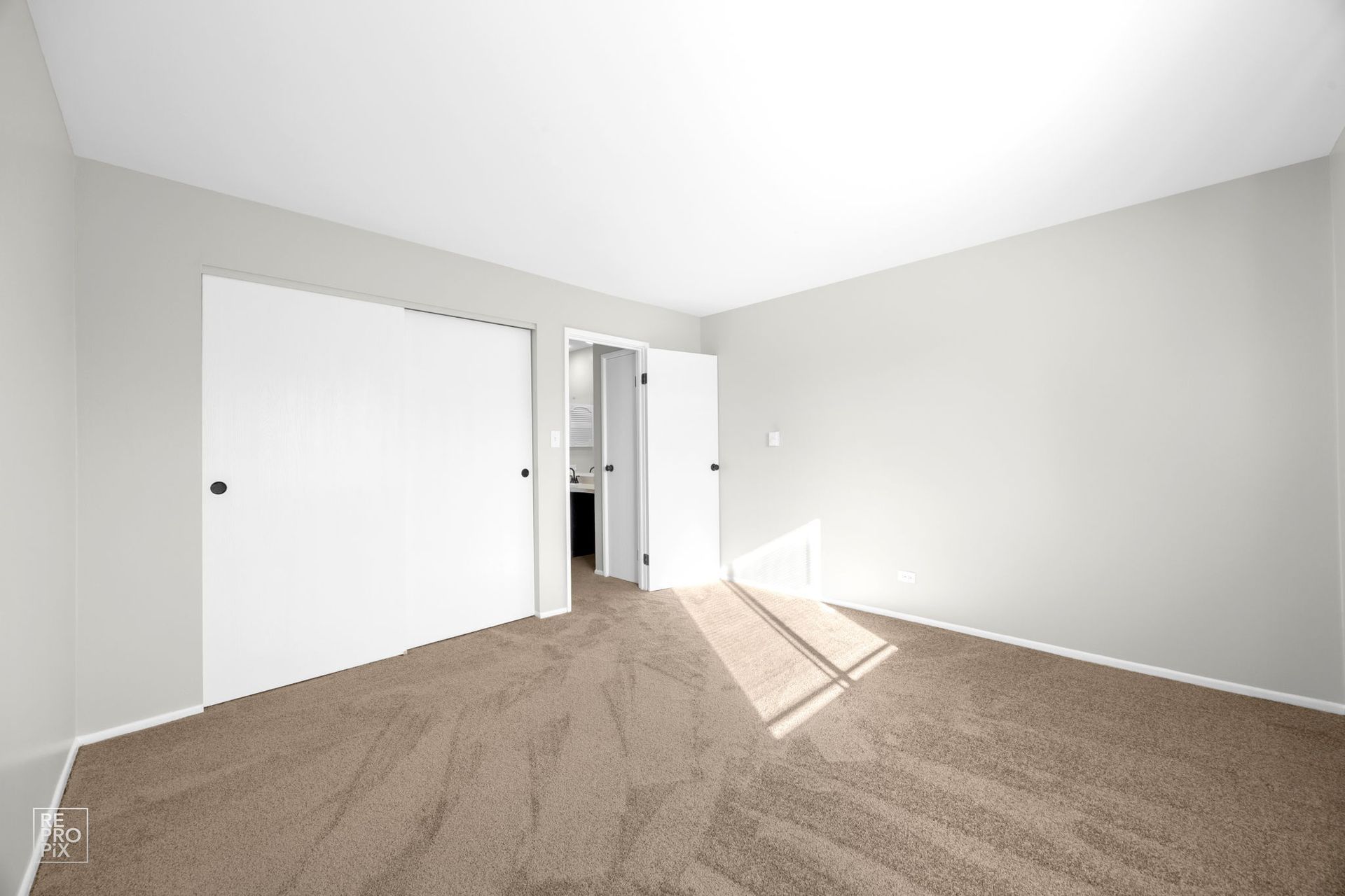 Empty bedroom with beige carpet, white closet doors, and light gray walls.
