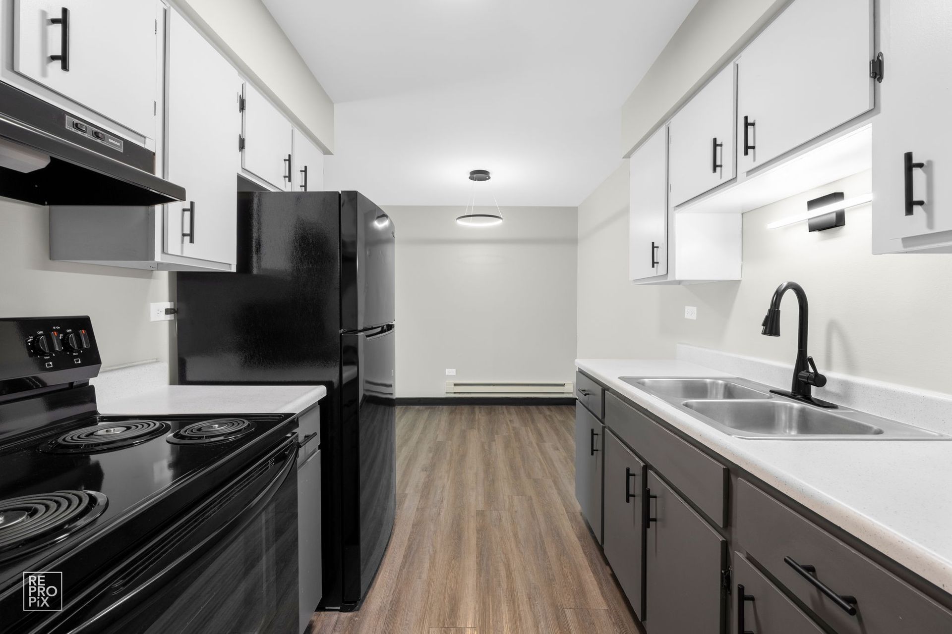 Kitchen with black appliances, white countertops, and cabinets; wooden floor, empty dining area.