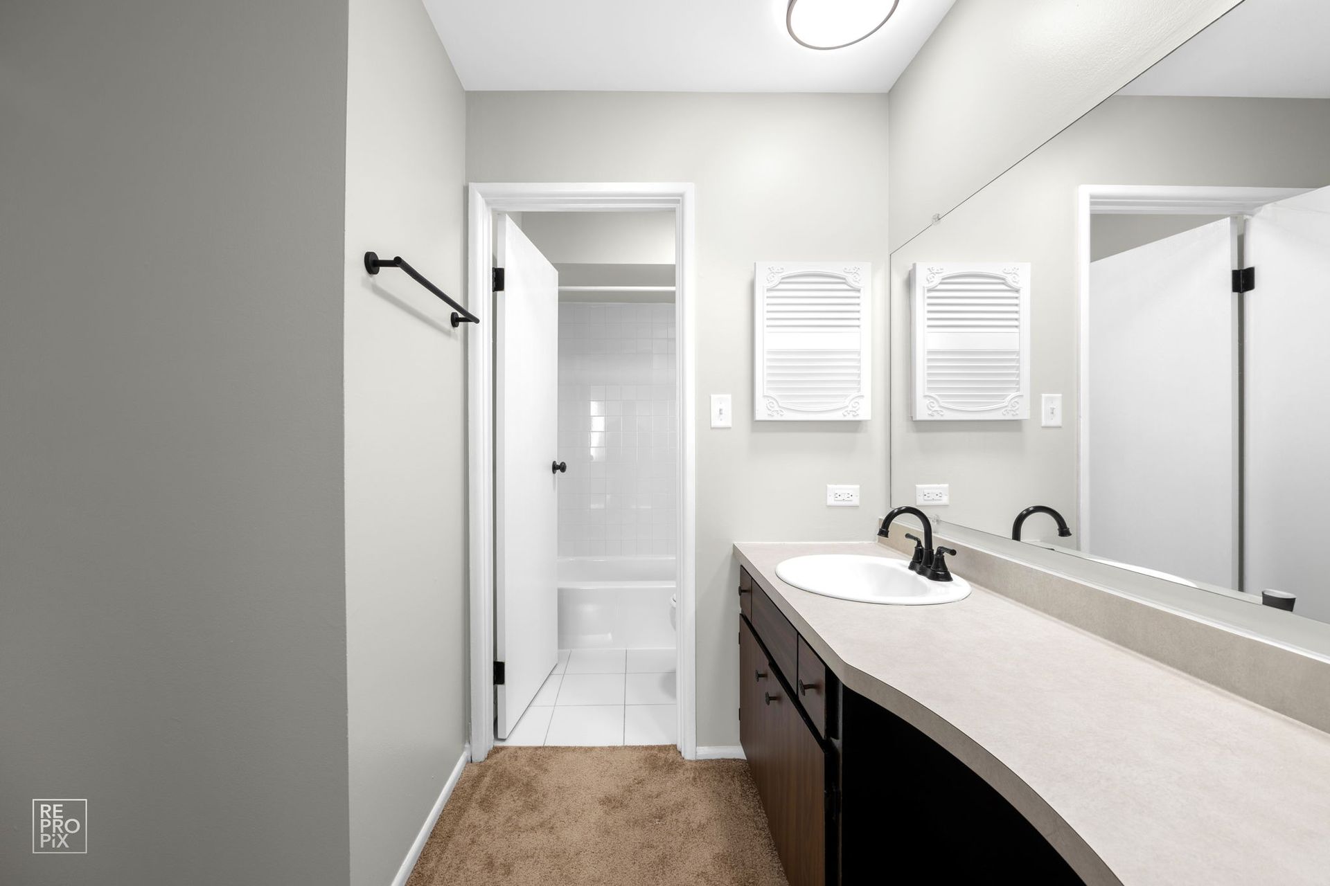 Bathroom with gray walls, dark vanity, long mirror, open door to shower, and light brown rug.