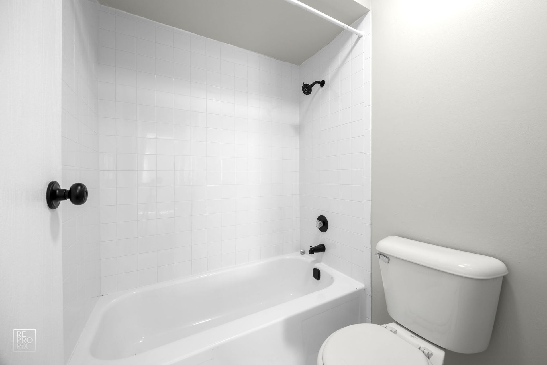 White bathroom with a tub and toilet, gray wall, black fixtures.