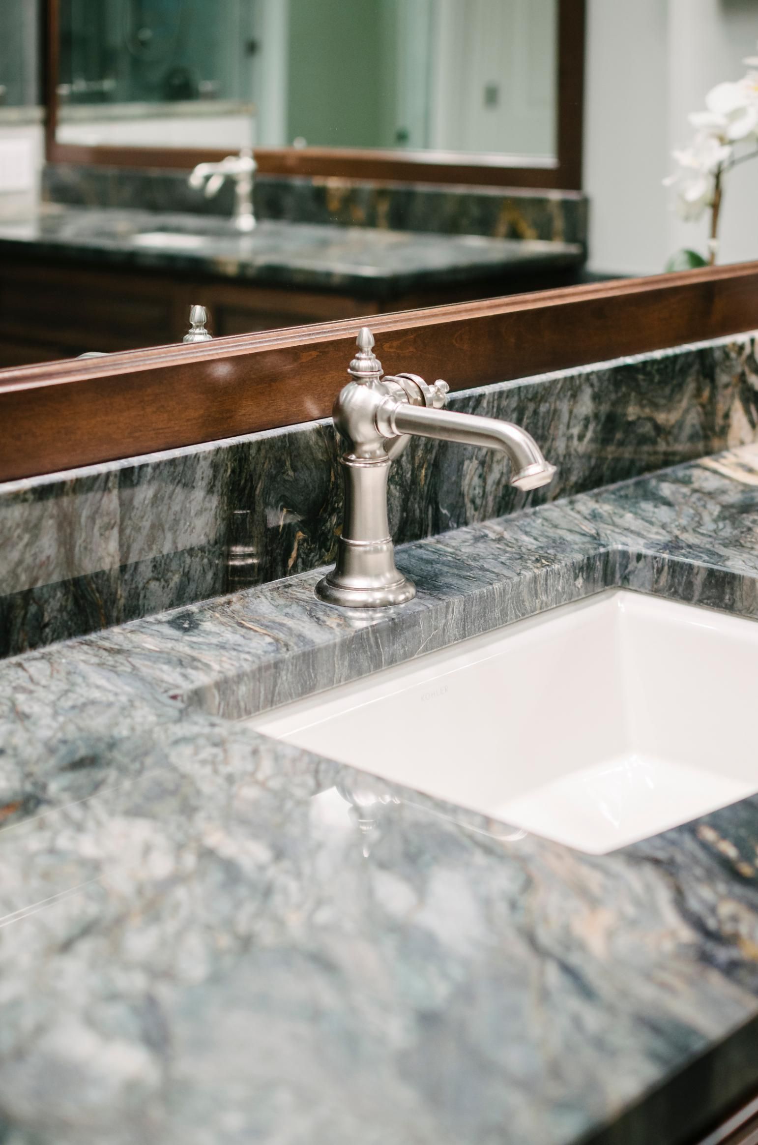 Bathroom vanity with ornate faucet on a marble countertop; a white sink and mirror are also visible.