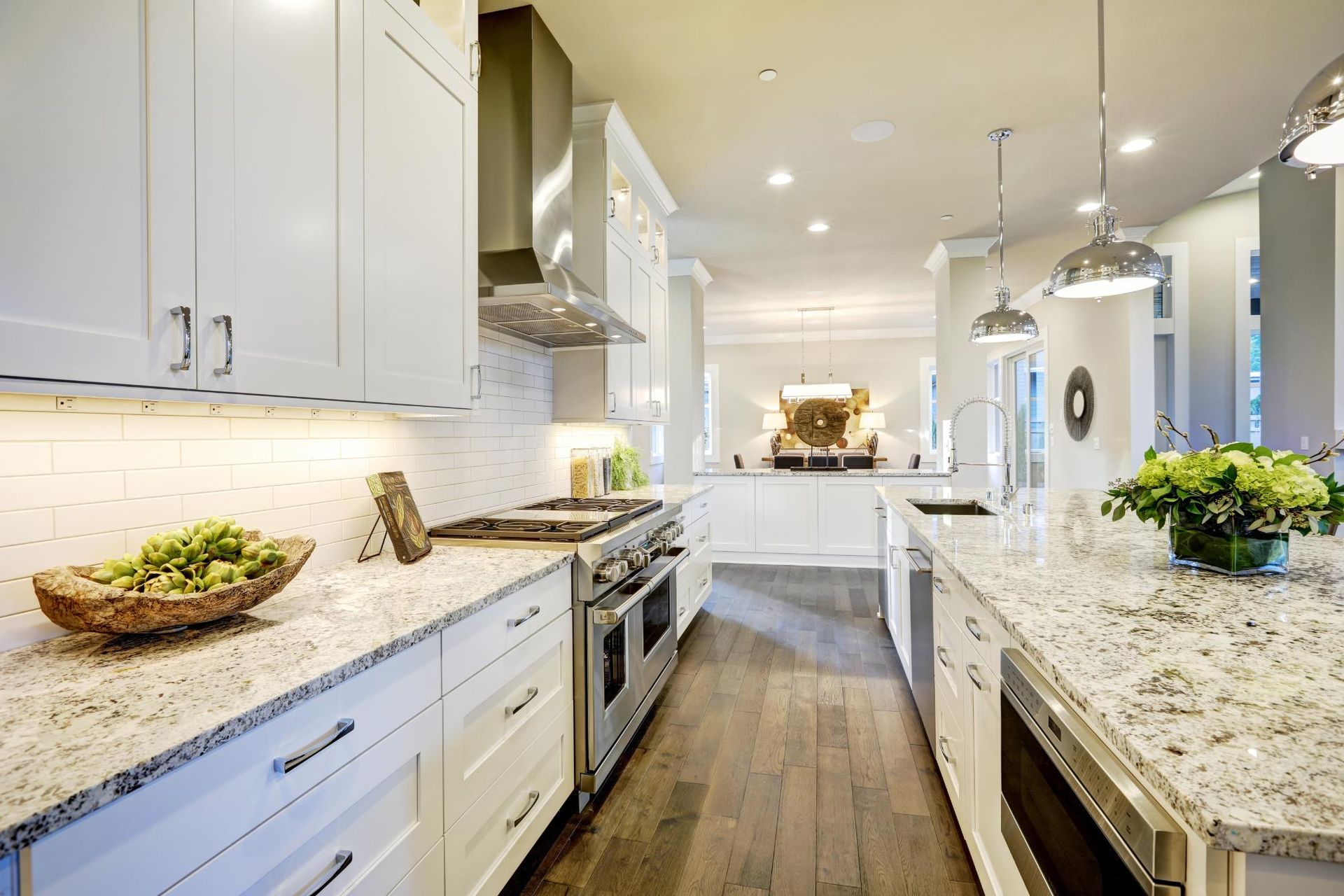 A modern, bright white kitchen with granite countertops, stainless steel appliances, and wood flooring.