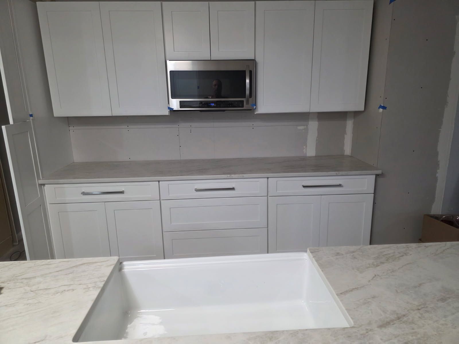 White kitchen cabinets with a built-in microwave and countertop with a large sink.
