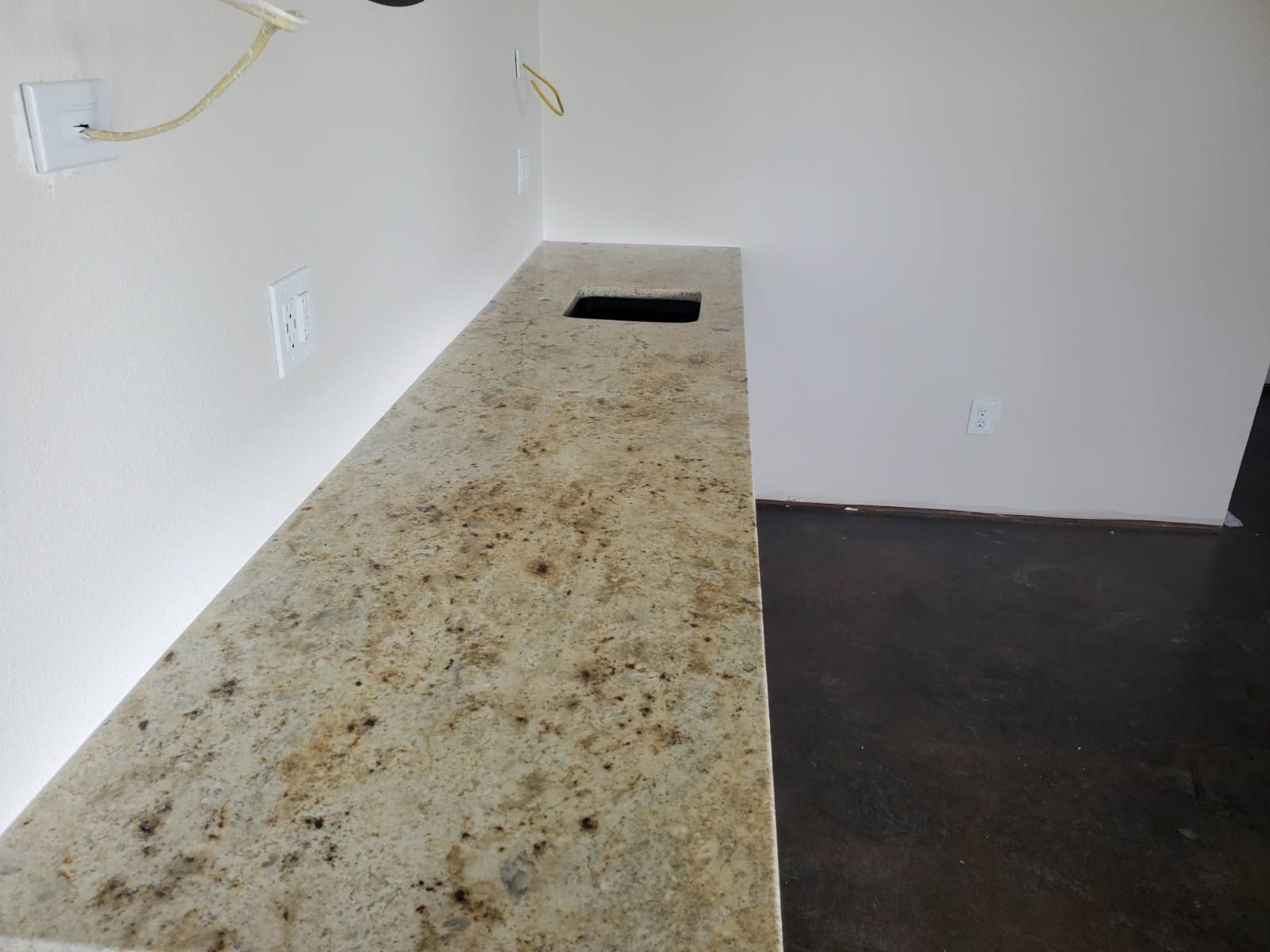 Granite countertop with a sink cutout against a white wall; dark floor.