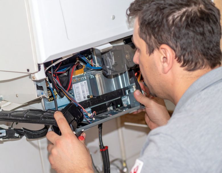 Man repairs a boiler, holding tools, looking at the open components.
