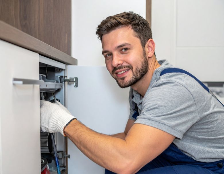 Man in work clothes fixing cabinet wiring, smiling.
