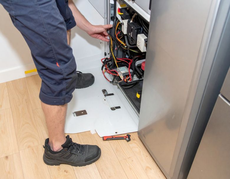 Person in blue pants working on electrical cabinet, indoor setting.