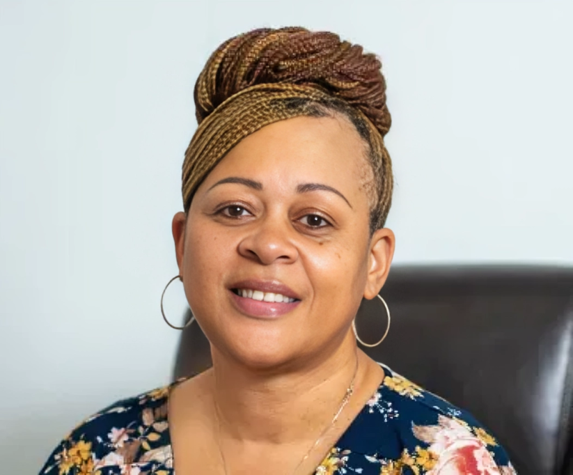 Woman with braided updo smiling, wearing hoop earrings and a floral top.