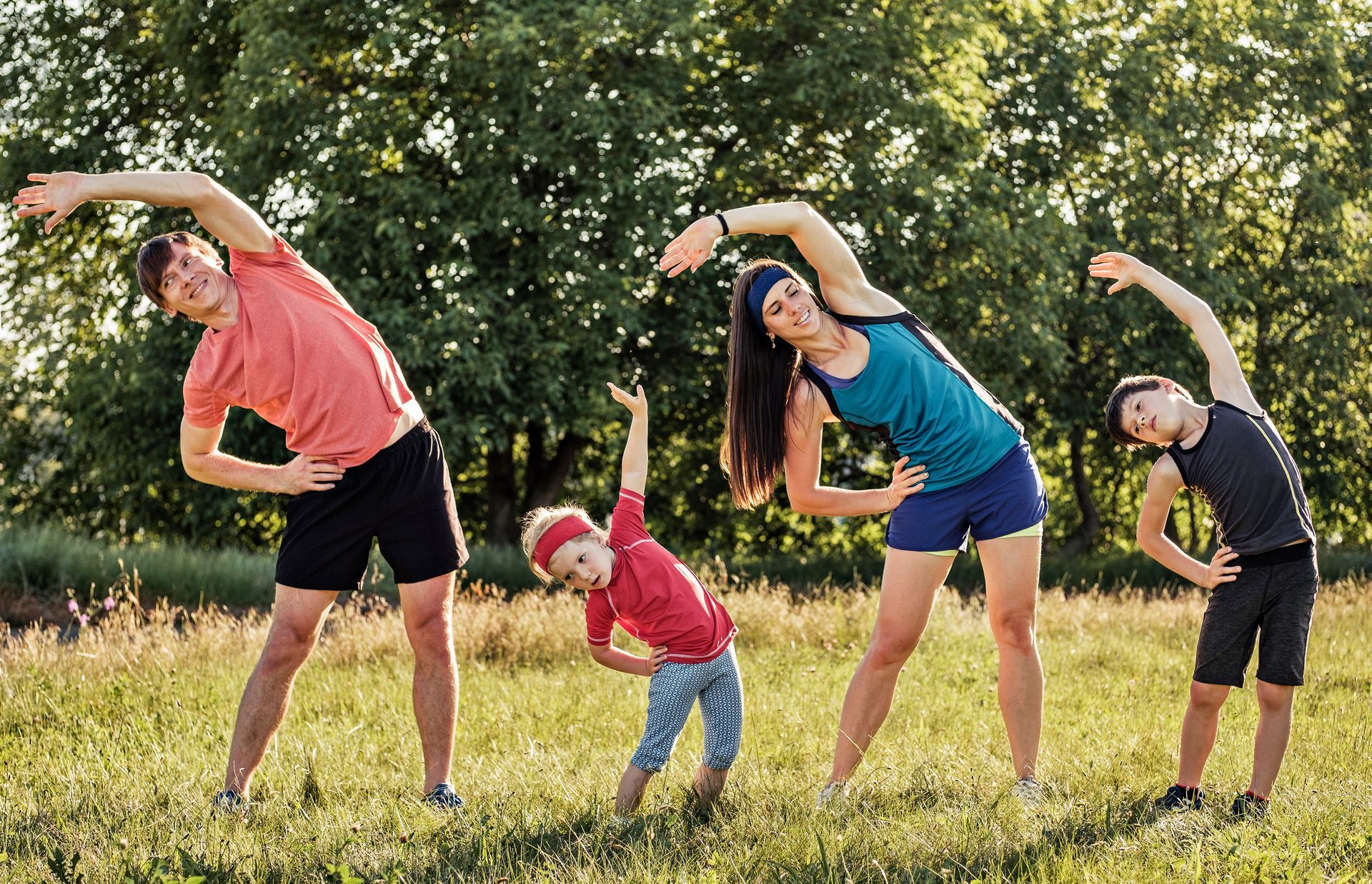 Family exercising outdoors, side bends. Sunny green field, adults and children.