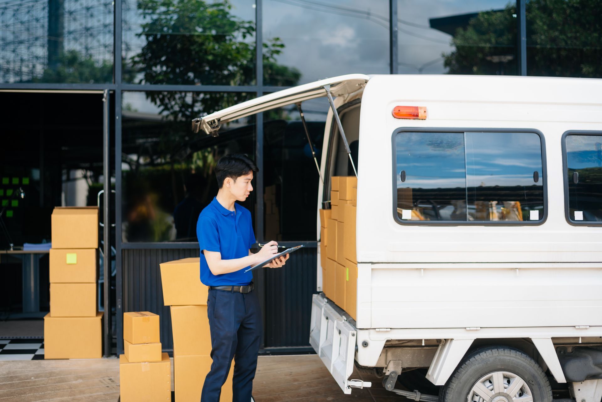 Delivery person with clipboard loading boxes into a white truck outside a building.