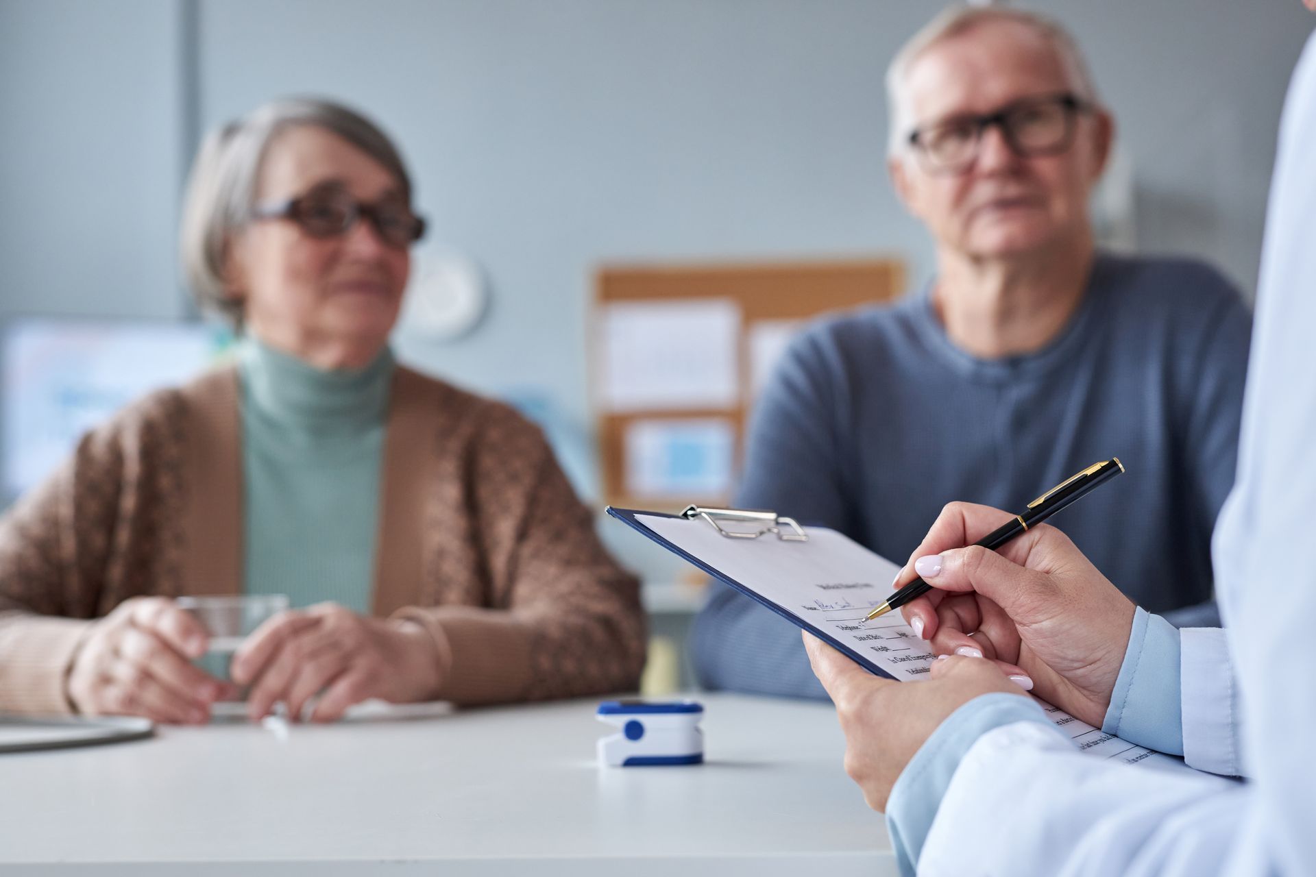 Doctor taking notes while consulting with an older couple in a medical office.