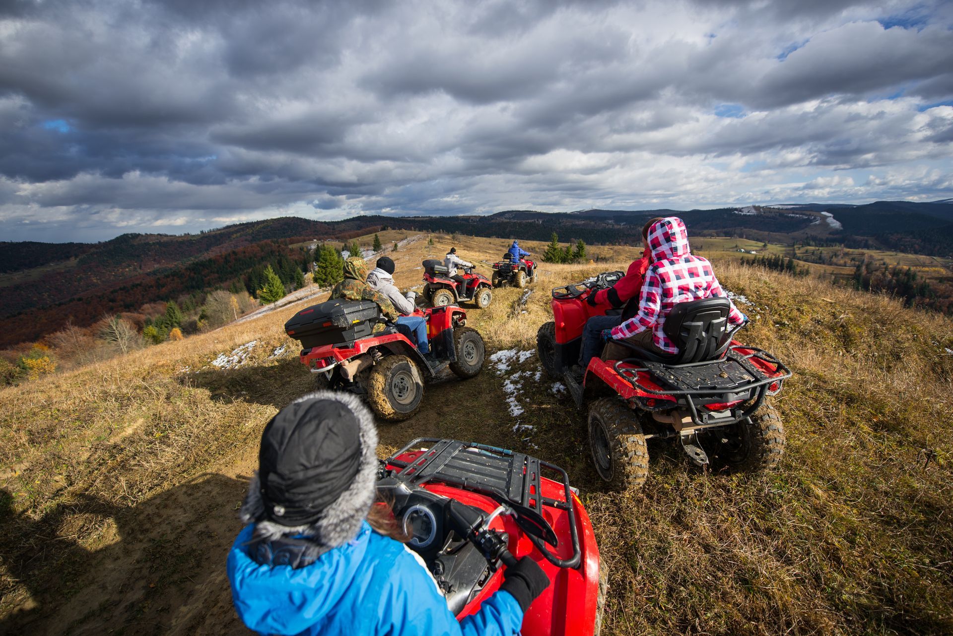 ATV riders on a grassy hilltop under a cloudy sky.