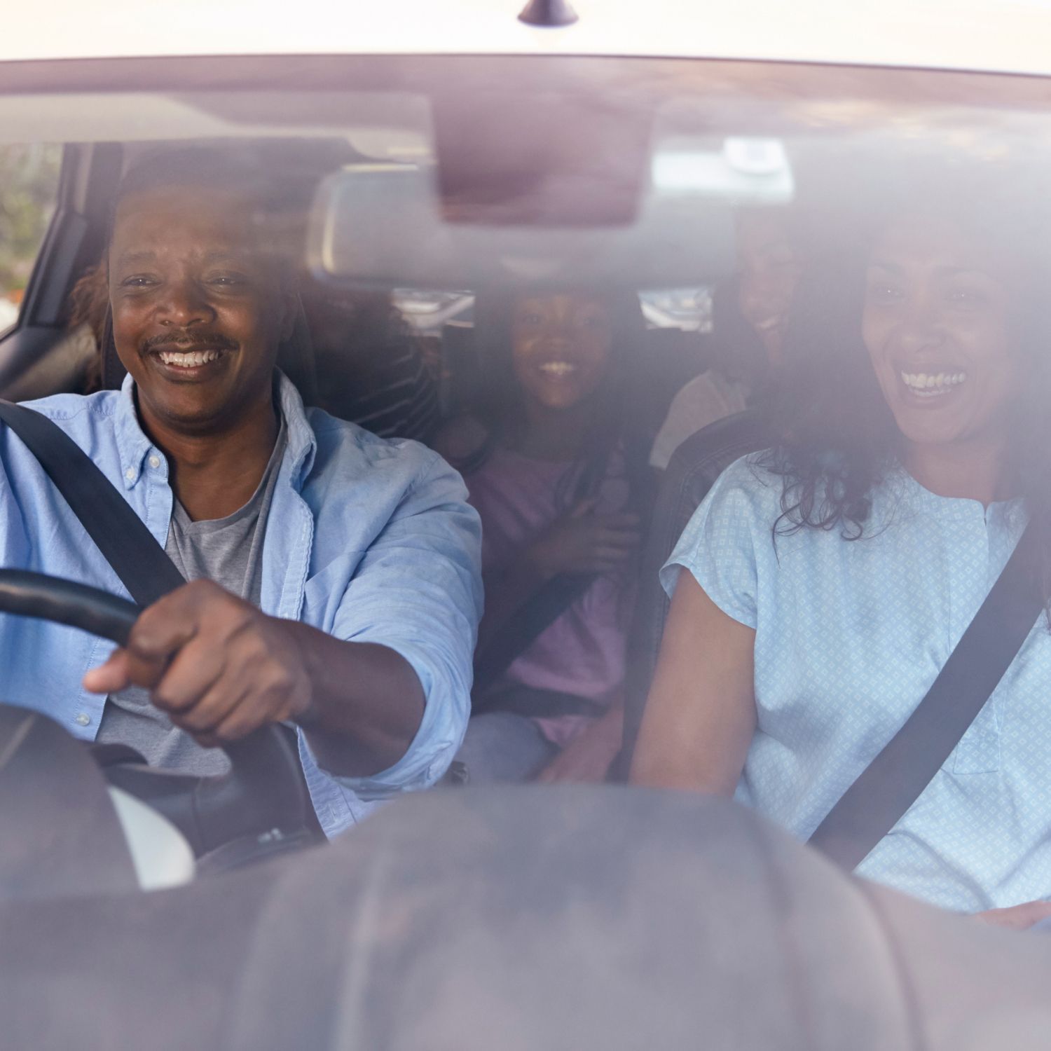 Family of four smiling inside a car, wearing seatbelts.