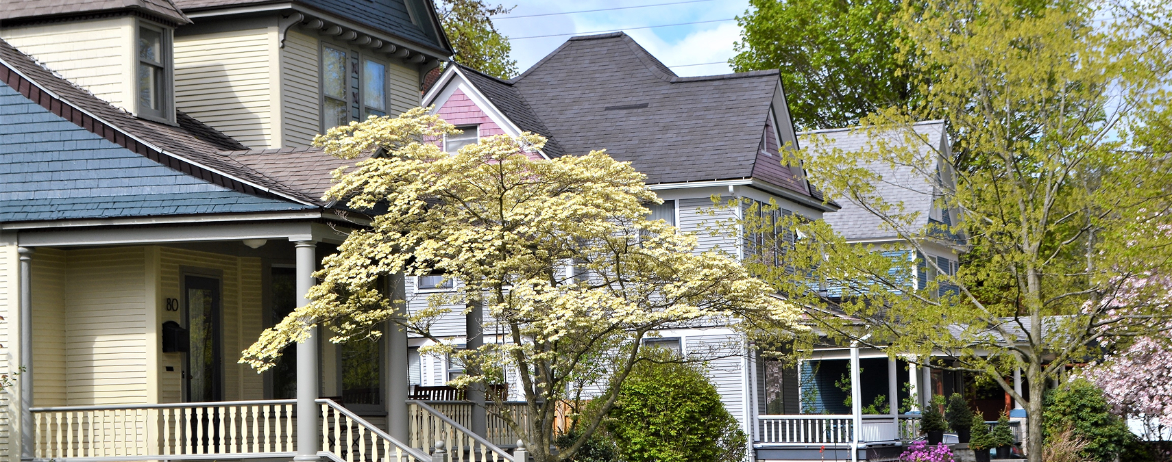 Row of Victorian houses with porches and blooming trees.