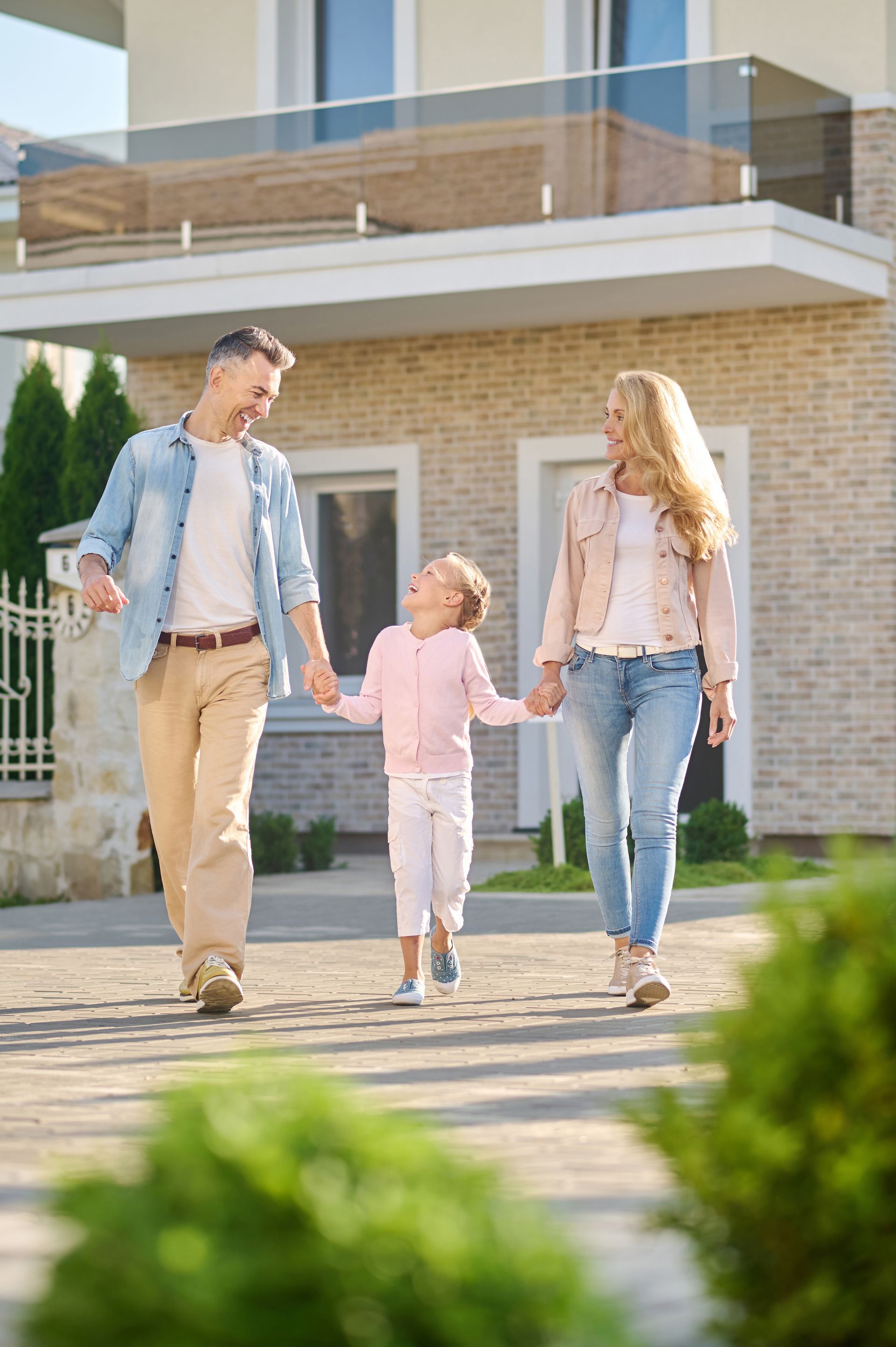 Family of three walking, holding hands in front of a house.