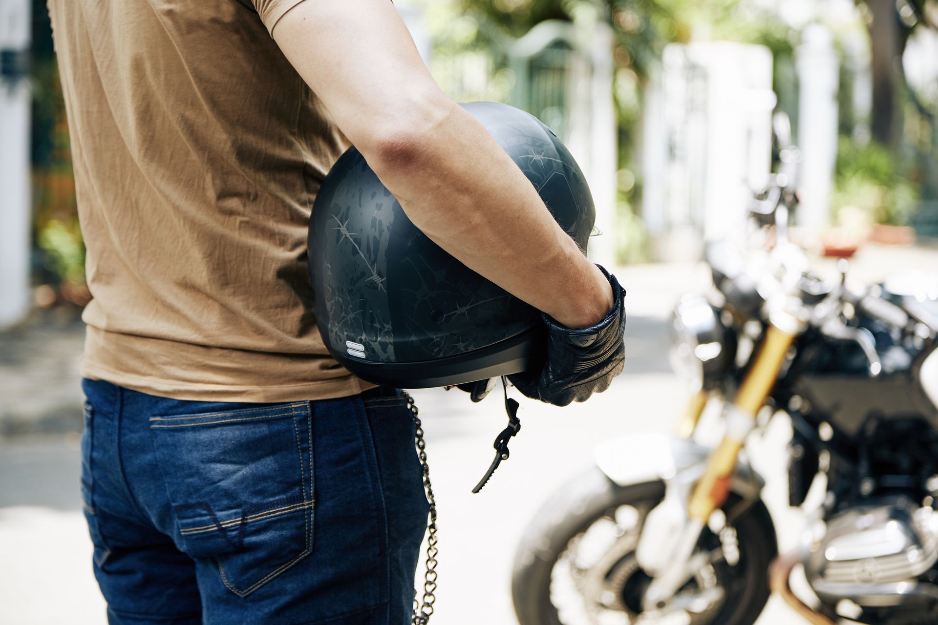 Person holding a black motorcycle helmet, standing near a motorcycle.