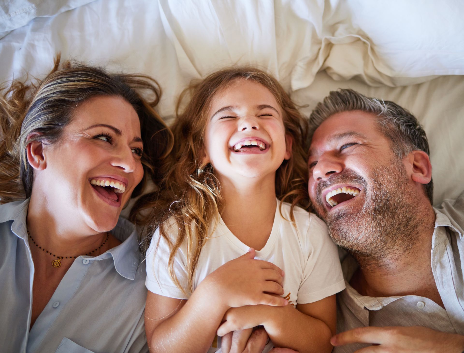 Family laughing together on a bed, smiling faces close together.
