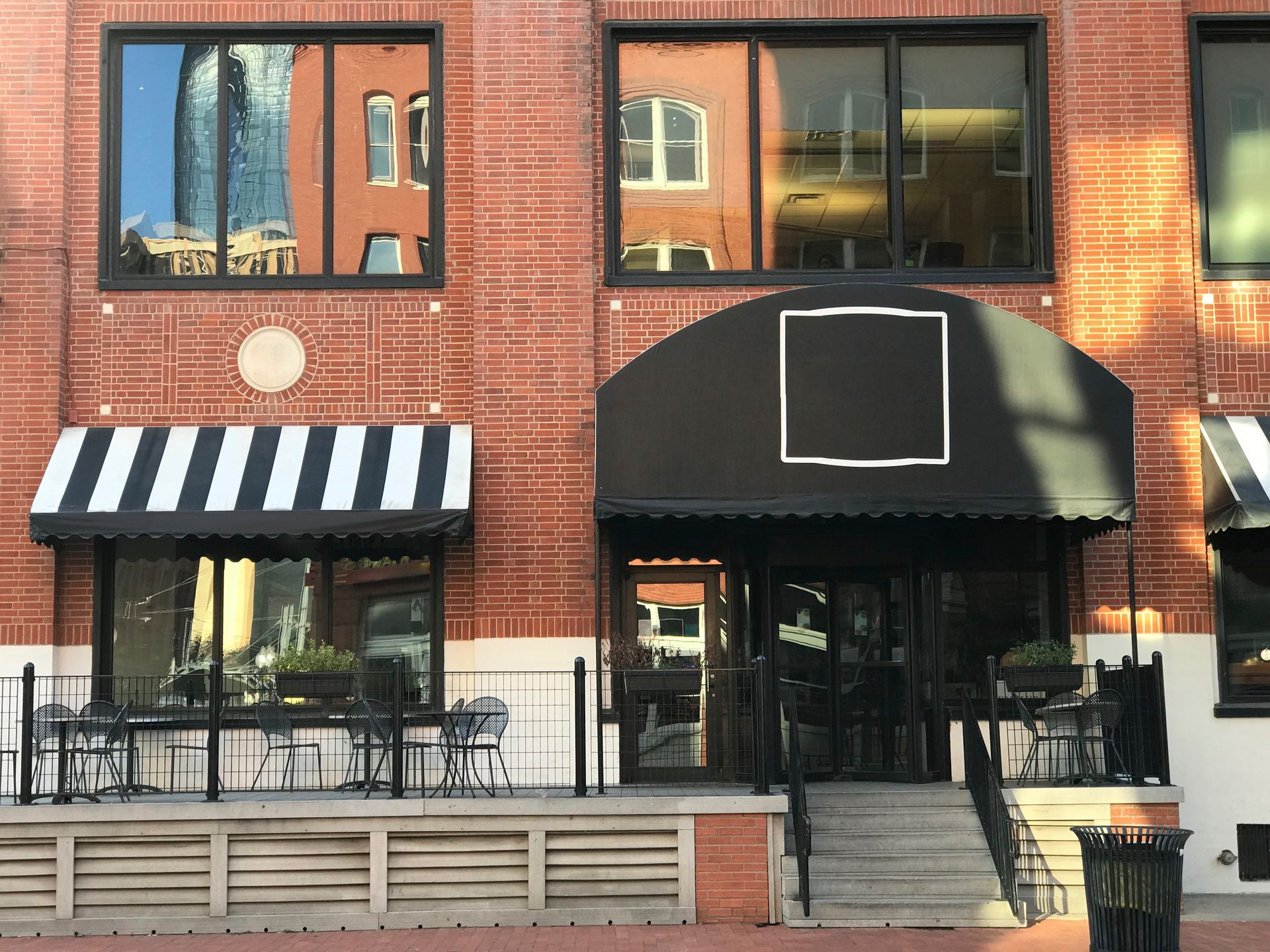 Red brick building with black awnings over doors and windows; outdoor seating.
