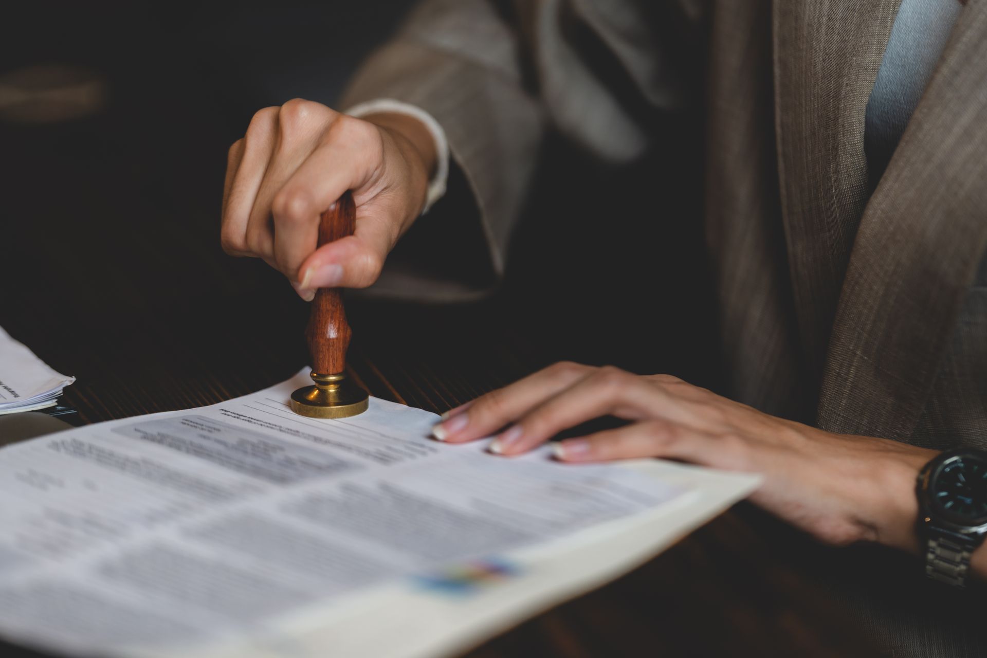 Person stamping a document with a wooden handle stamp, inside a dimly lit room.