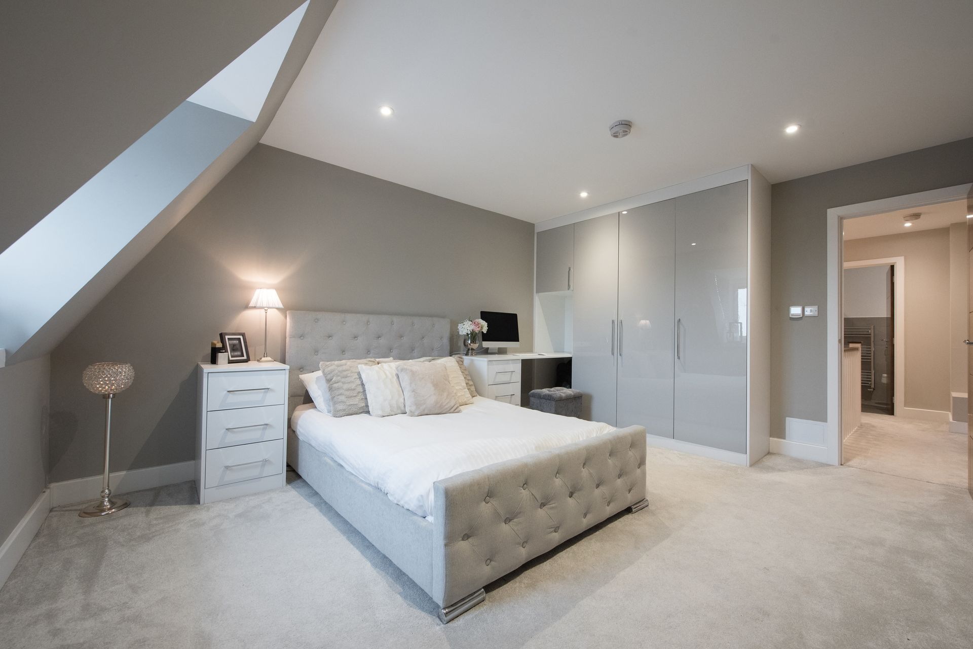 Bedroom with a grey bed, dresser, and a slanted ceiling with a window.
