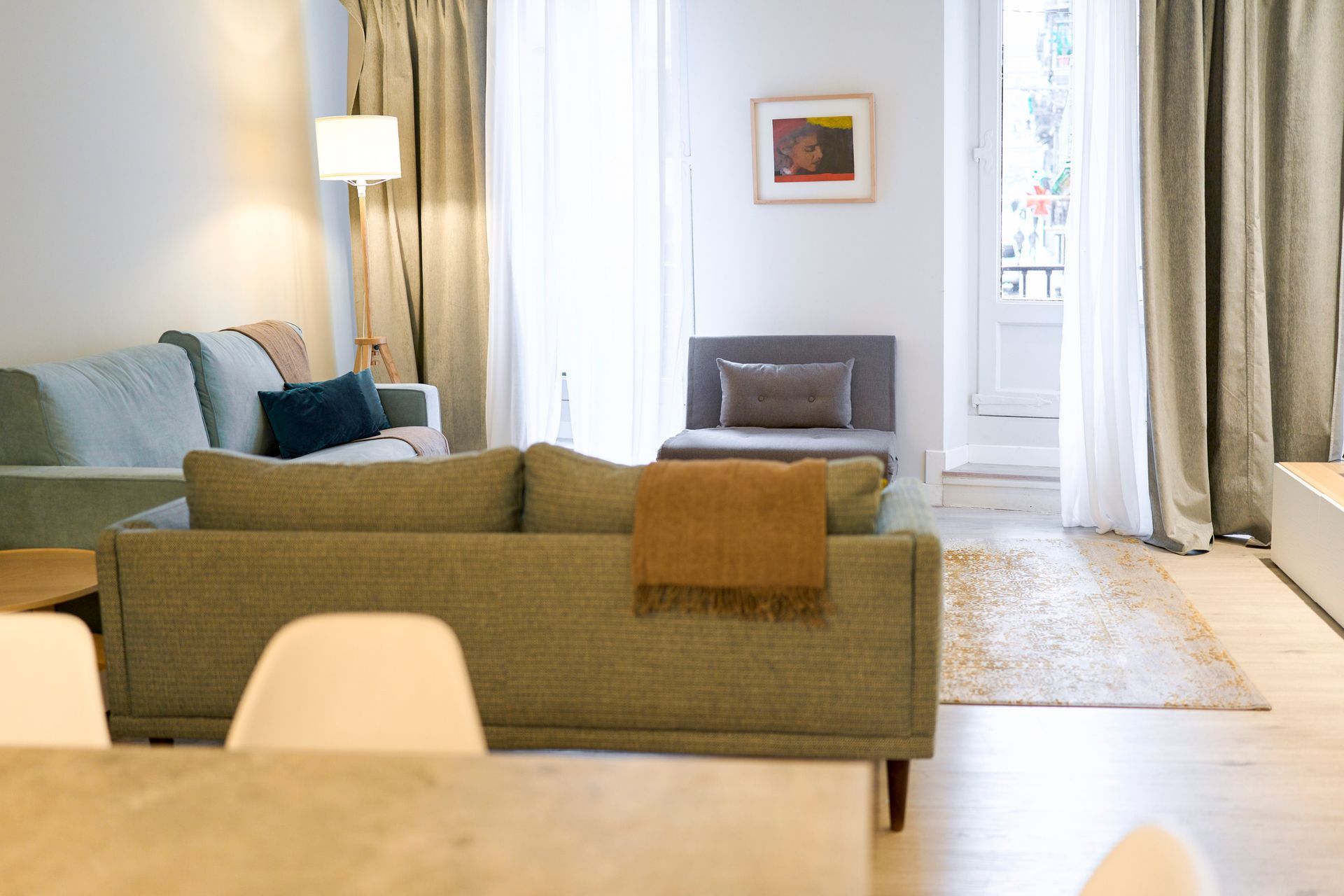 Living room with two green sofas, light curtains, and a view to a balcony.